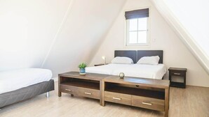 Un dormitorio con una cama, mesitas de noche, una ventana y una planta pequeña.