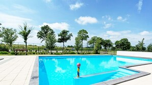 Una piscina rectangular con superficie de agua azul cristalina, rodeada por un solárium con baldosas y una valla.