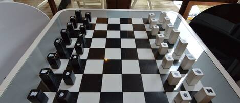 A checkered game board with black and white pieces, set on a table in a room with large windows.