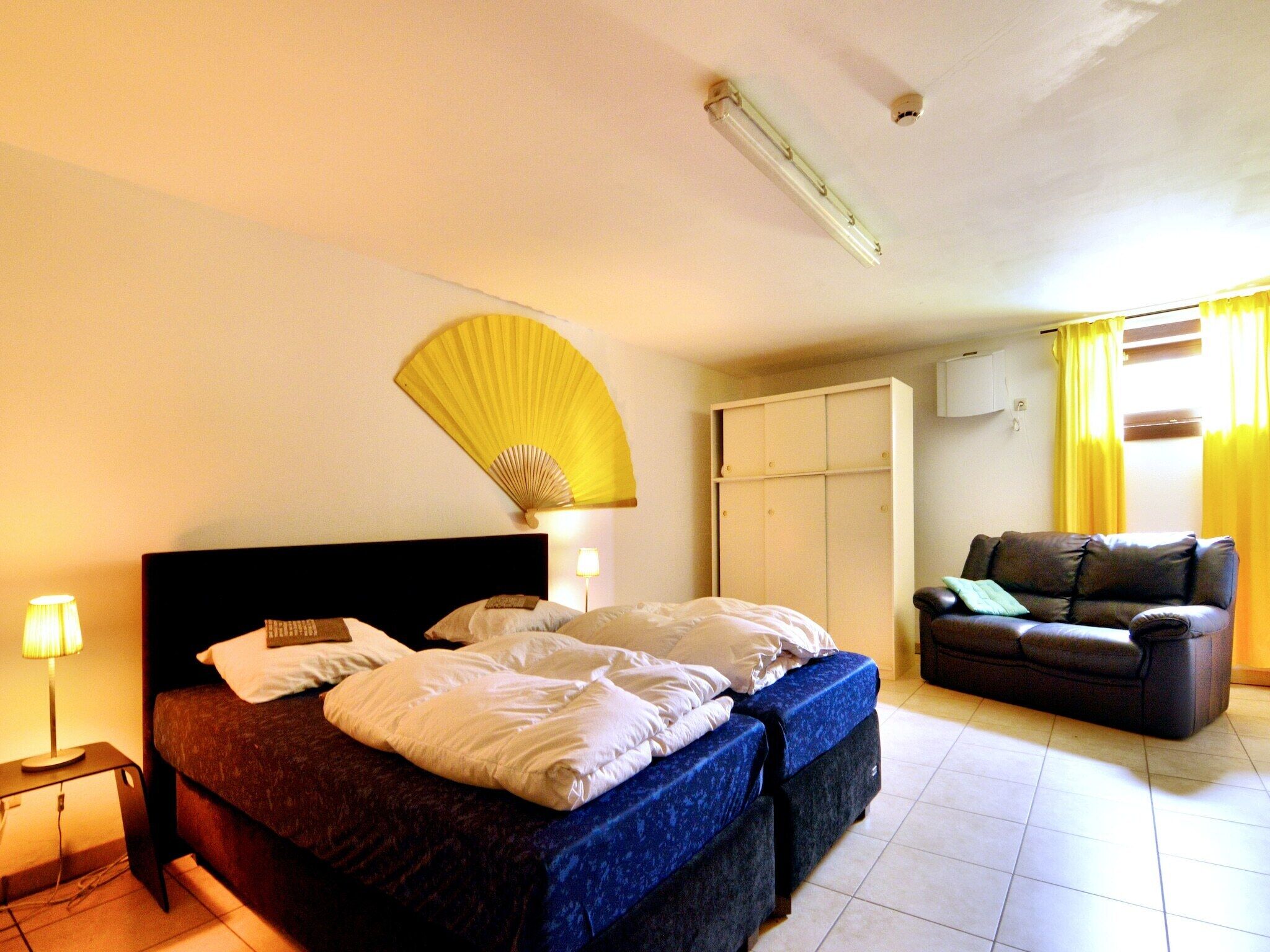Habitación de hotel con cama, ventilador, sofá y armario.