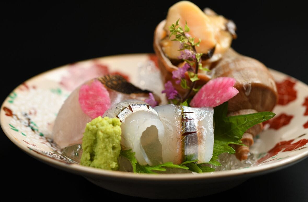 A plate with various seafood items, including fish and possibly shrimp, garnished with herbs and flowers.
