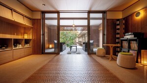Un interior moderno con un sendero central que lleva a un espacio exterior, estanterías de madera y un conjunto de asientos.