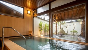 Un onsen japonés tradicional con una terraza de madera, vistas al jardín y una cuenca de piedra.