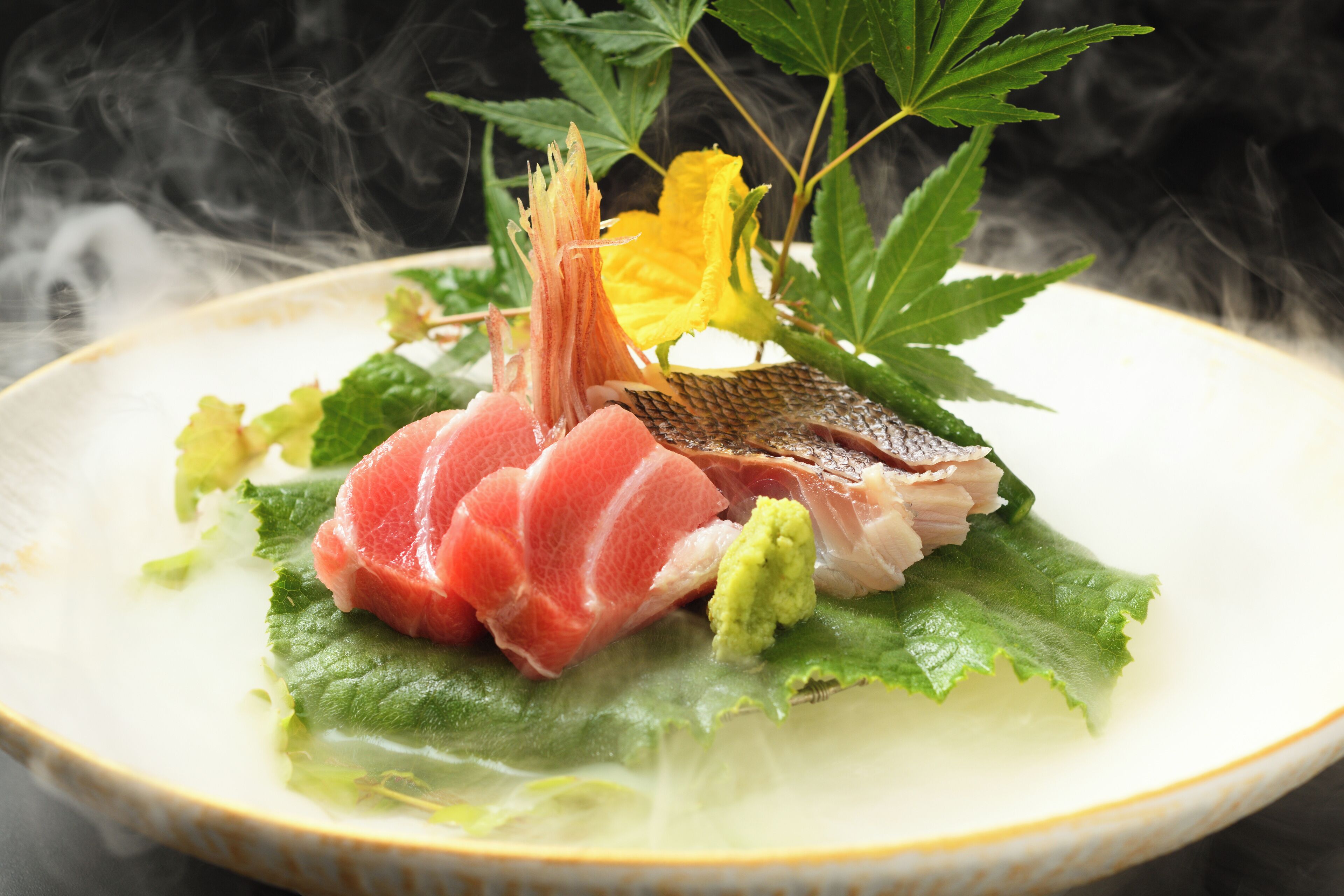 Un plato de sashimi con hojas verdes y una flor amarilla.