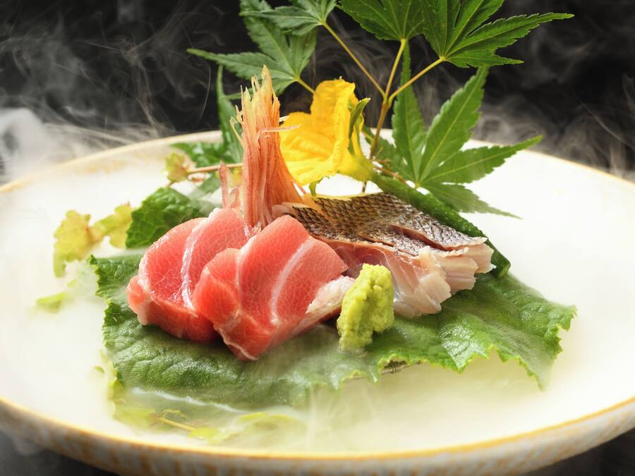Un plato de sashimi con hojas verdes y una flor amarilla.