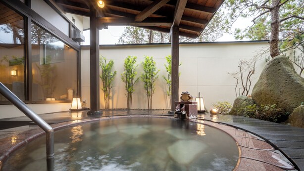 Un área de aguas termales con una terraza de madera, una bañera de piedra caliente y una escultura de piedra.