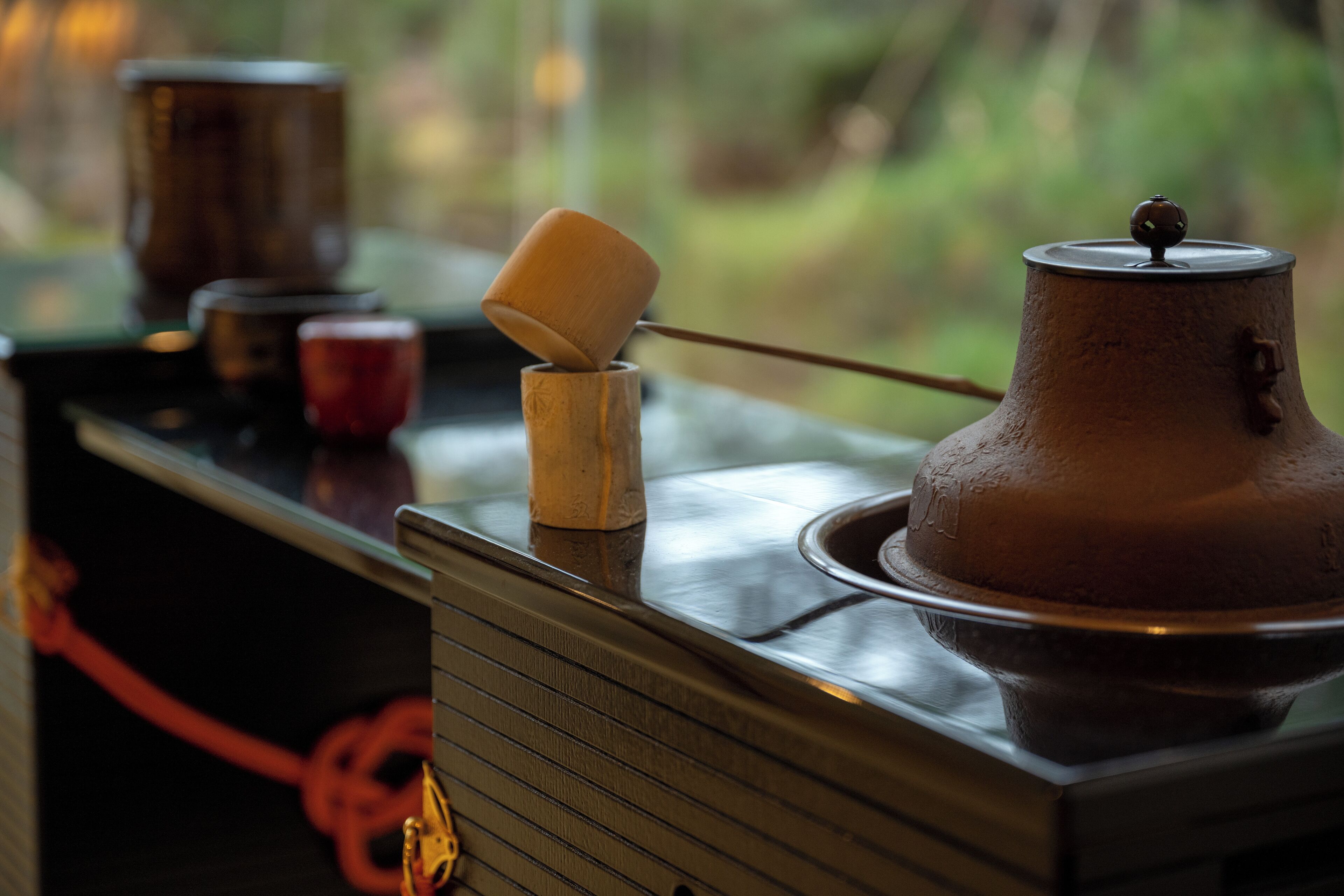 Una mesa de madera con una olla de metal, una taza de madera y una taza roja.