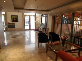 Um hall espaçoso com piso de azulejos, balcão de recepção e área de estar com cadeiras e mesa.