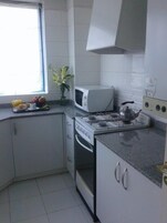 Cozinha compacta com armários brancos, micro-ondas, fogão e chaleira.
