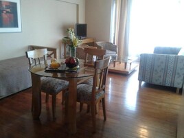 Uma sala de jantar com mesa de vidro, cadeiras de madeira e um sofá ao fundo.