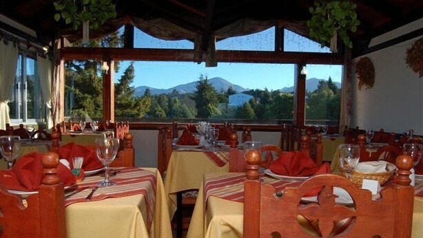 A restaurant with tables set for dining, wooden chairs, and a view of mountains through large windows. - Ruca Cheli Village Ski Hotel (San Carlos de Bariloche)