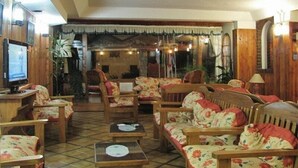 A cozy living room with wooden furniture, a television, and a decorative archway. - Ruca Cheli Village Ski Hotel (San Carlos de Bariloche)
