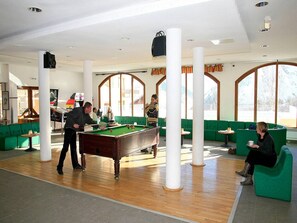 A billiards room with a pool table, green sofas, and a large window.