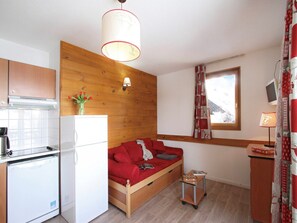 A compact room with a kitchenette, a wooden wall, a sofa, and a small table with a book.