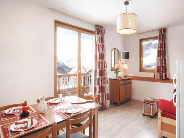 A dining area with a table set for two, a mirror, a television, and a view of snowy mountains through the windows.