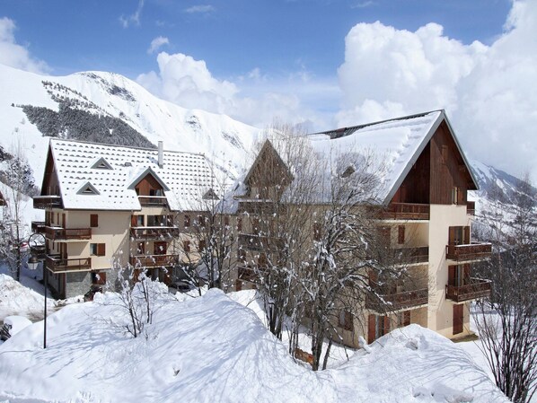 A snow-covered mountain resort with multi-story buildings, including a chalet and a hotel with balconies.