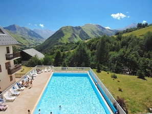 Una piscina con vista sulle montagne, un edificio con un balcone e poltrone relax.