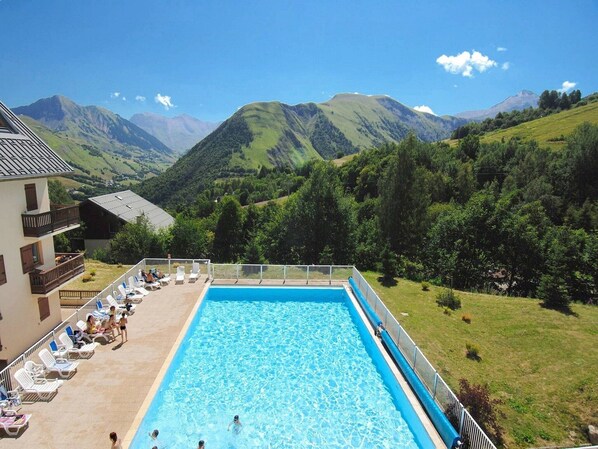 Une piscine avec vue sur les montagnes, un bâtiment doté d’un balcon et de chaises longues.