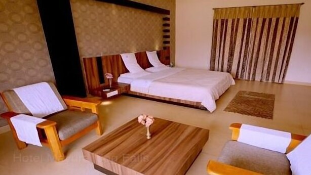 Una habitación de hotel con una cama, dos sillones, una mesita de centro y una mesita de noche.