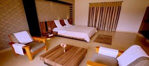A hotel room with a bed, two armchairs, a coffee table, and a nightstand. - KSTDC Hotel Mayura Gerusoppa (Sagara)