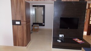 Una sala de estar moderna con un televisor de pantalla plana montado en una pared de madera oscura, un taburete pequeño y una revista sobre el mueble de televisión.