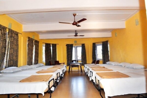 A hotel room with two beds, a ceiling fan, and a window with curtains. - KSTDC Hotel Mayura Gerusoppa (Sagara)