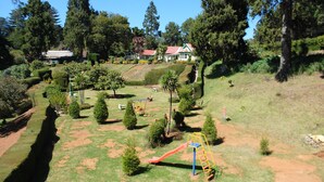 Un parque con juegos infantiles, setos cuidadosamente recortados y un edificio con tejado rojo al fondo.