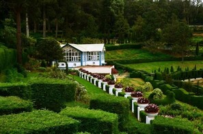 Una casa rodeada de setos cuidados y un jardín con macetas de flores ordenadas.