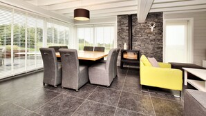 A modern living room with a stone fireplace, a dining table with chairs, and a yellow armchair. - Holiday home suitable for families with sauna (Wilogne)