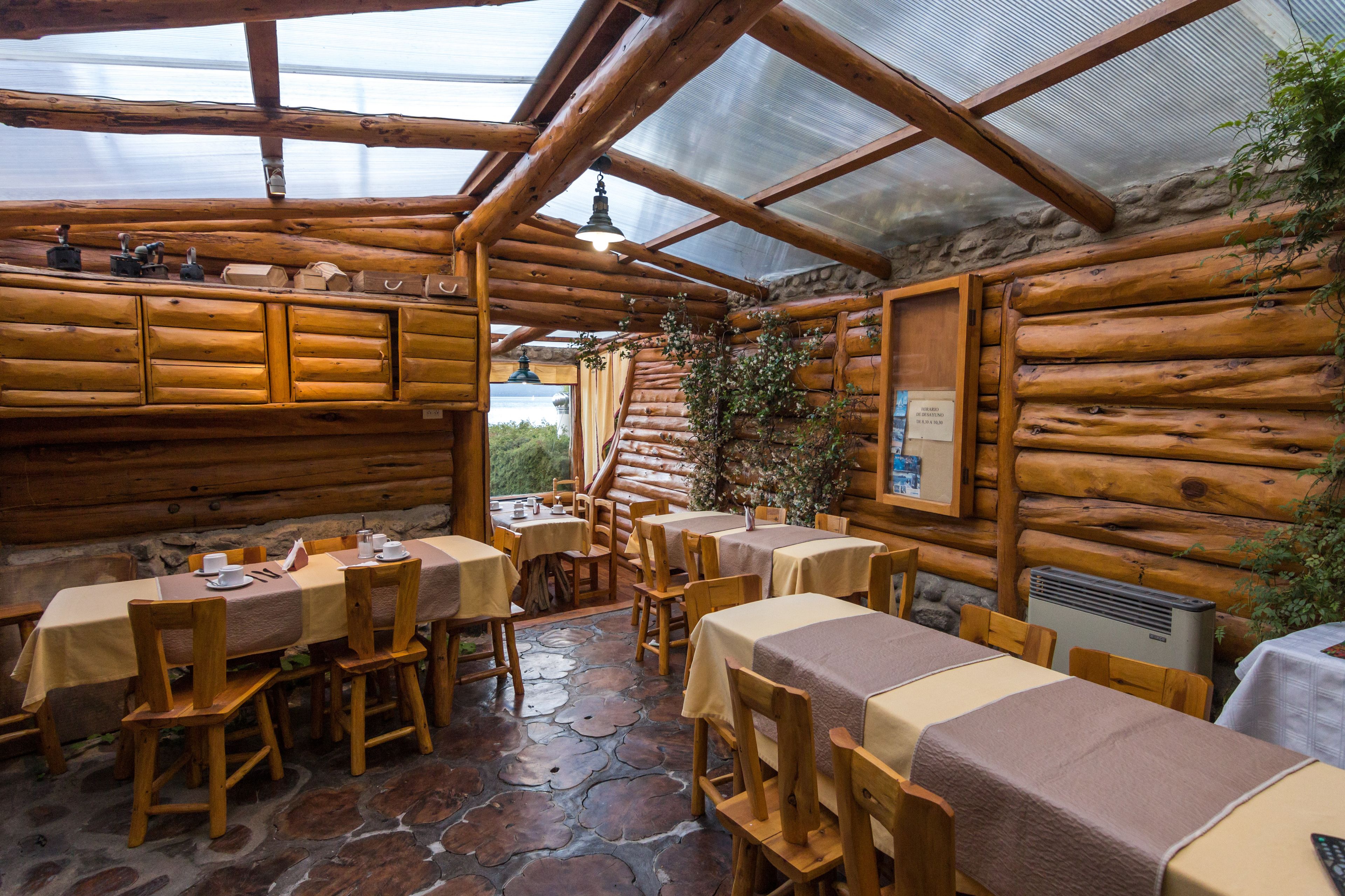 A rustic wooden dining area with tables and chairs, a stone floor, and a glass ceiling.