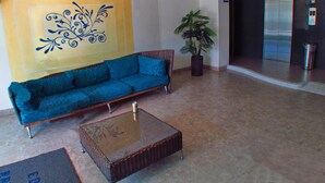 A lobby with a blue sofa, a wicker coffee table, a potted plant, and a wall with a decorative design. - Apartamentos Suiteline Plus - Cerca al Mar (Santa Marta)