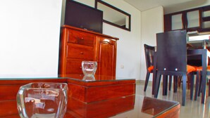 A dining area with a glass-top table, wooden chairs, and a wooden cabinet with drawers. - Apartamentos Suiteline Plus - Cerca al Mar (Santa Marta)