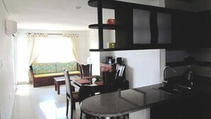 A compact kitchen with a dining area, a built-in shelf unit, and a window with curtains. - Apartamento Mar Azul - Smr143a (Santa Marta)