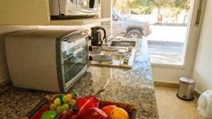 A kitchen with a microwave, toaster, and a fruit basket on the counter. - Tower Rock Departamentos Estándar (Puerto Deseado)