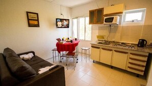 A compact living space with a kitchenette, a dining area with a red table, and a sofa with a blanket. - Tower Rock Departamentos Estándar (Puerto Deseado)