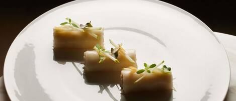 Un plato blanco con tres porciones de comida cuadrada, cada una adornada con hierbas verdes, sobre un fondo oscuro.