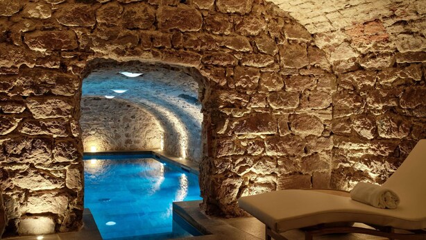 Un área de spa con paredes de piedra, una piscina y una silla de descanso.