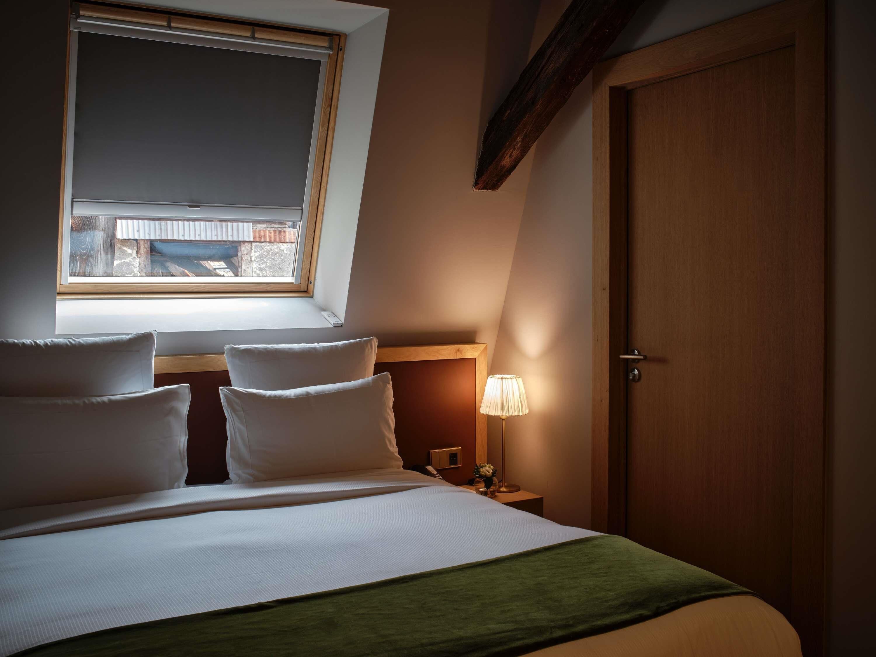 Ein Schlafzimmer mit Bett, Kissen, Nachttisch, Lampe, Fenster und Tür.