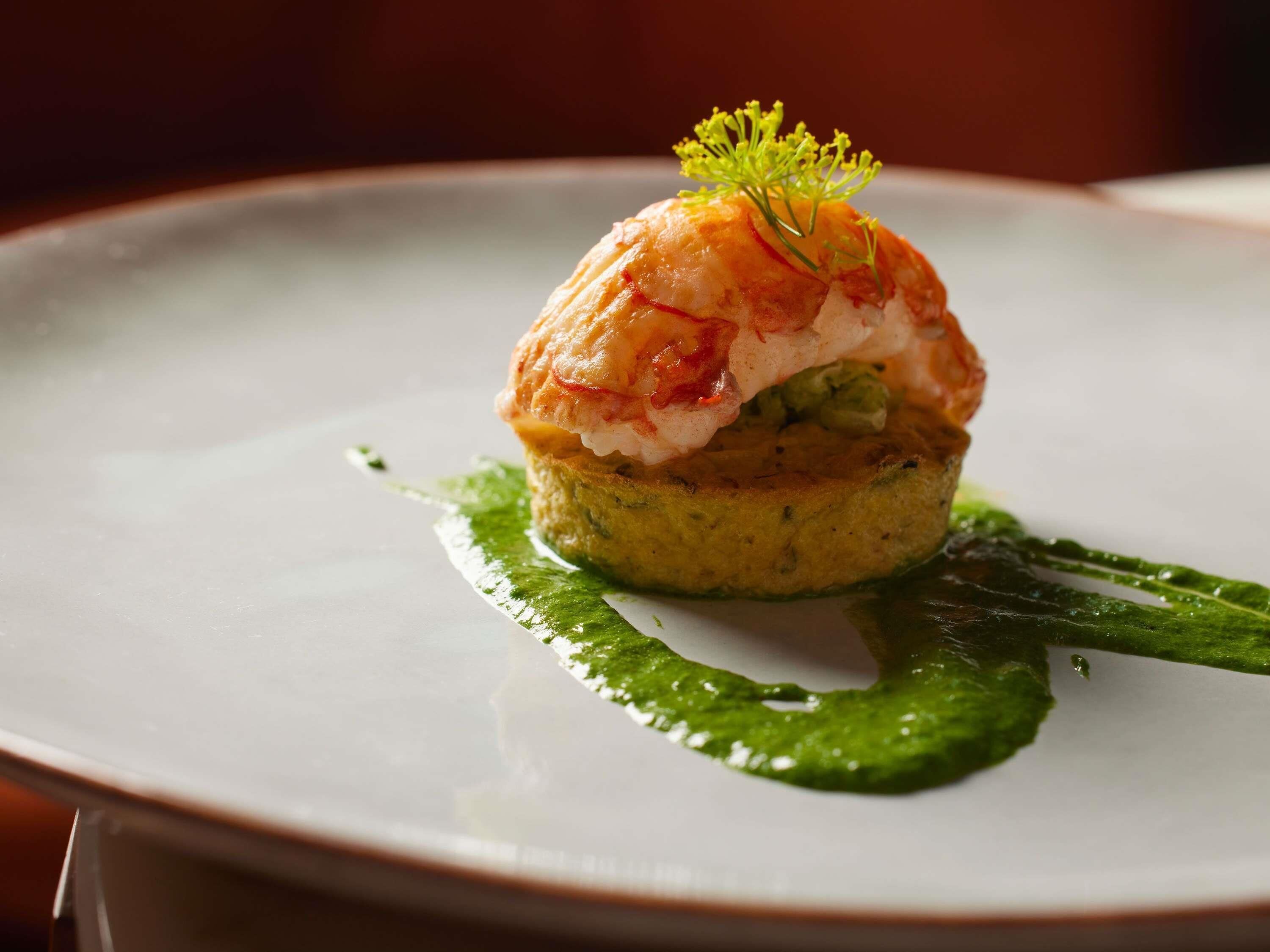 Een bord met een gerecht, mogelijk zeevruchten, gegarneerd met een groene saus en een kleine groene versiering.