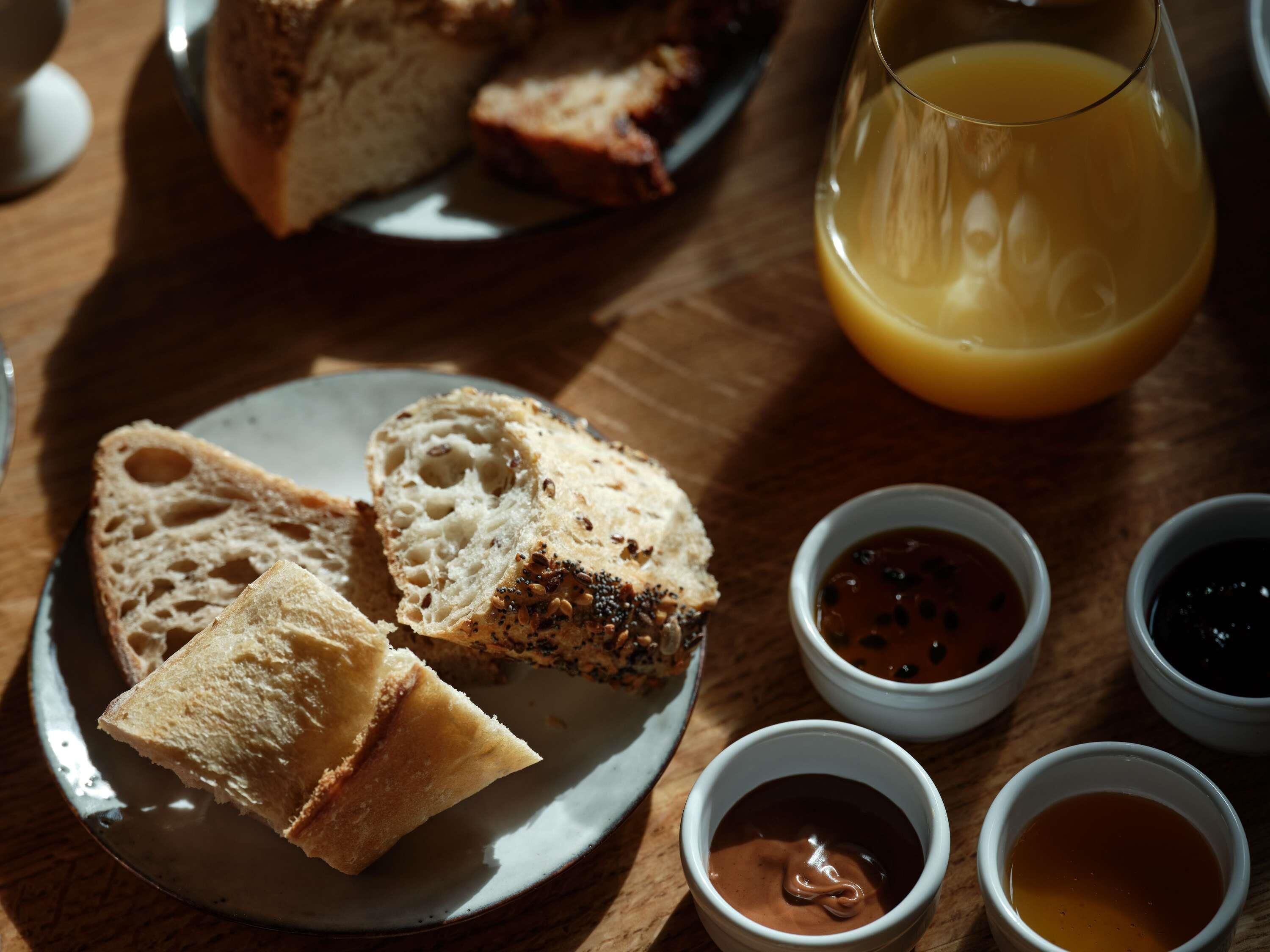 Une table mise pour le petit-déjeuner avec du pain, un verre de jus d’orange et de petits bols contenant des condiments.