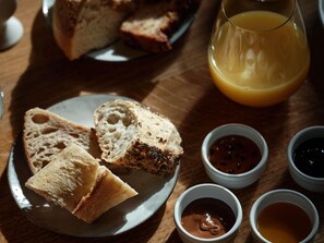 Desayuno con pan, un vaso de jugo de naranja y recipientes pequeños con condimentos.