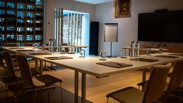 Une salle de conférence équipée d’une longue table, de chaises, d’un écran de projection et d’un mur avec des étagères remplies de casques.