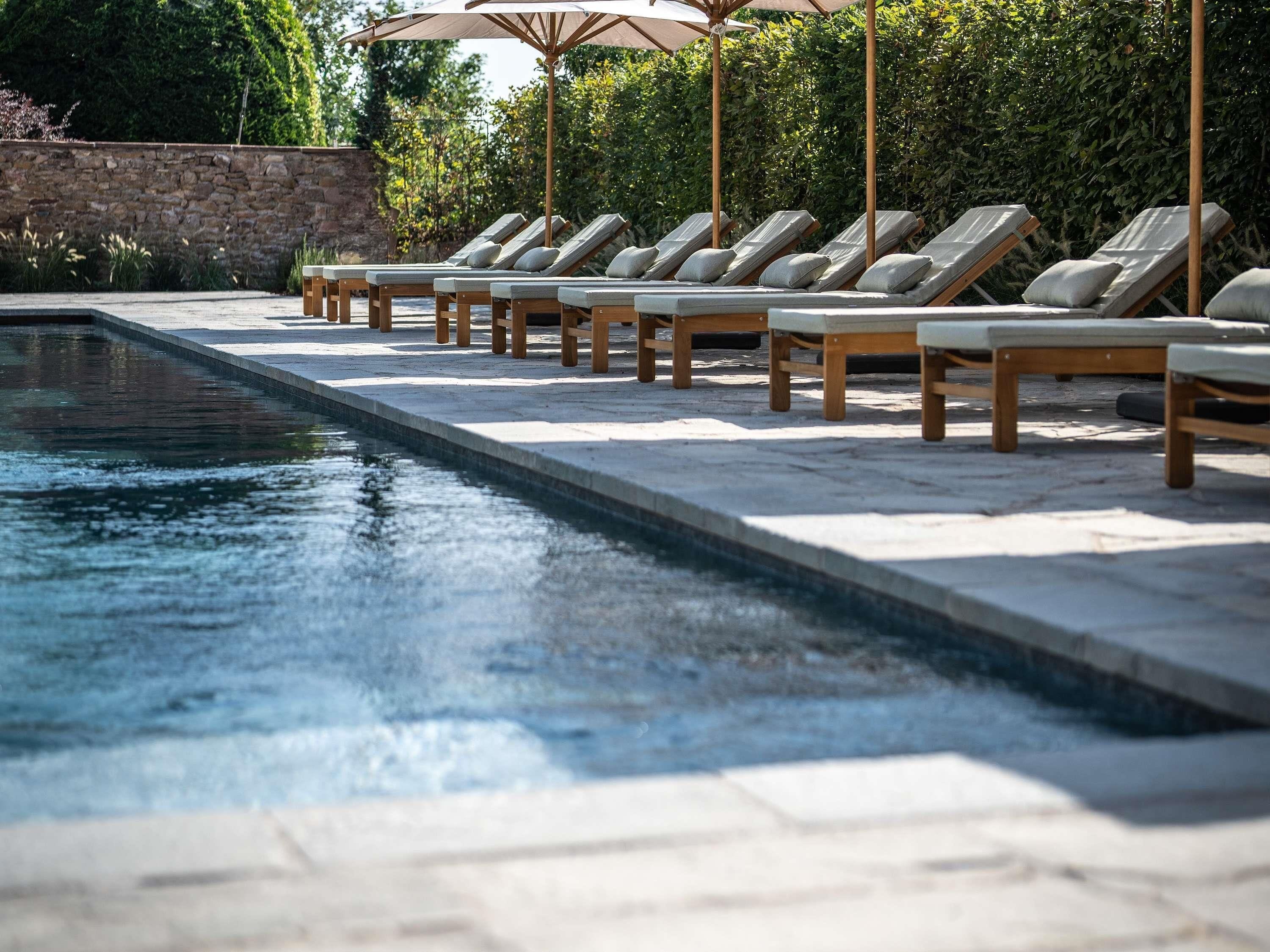 Zona de piscina con sillas de descanso y sombrillas.
