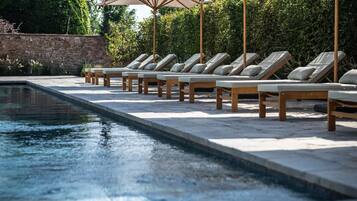 Zona de piscina con sillas de descanso y sombrillas.