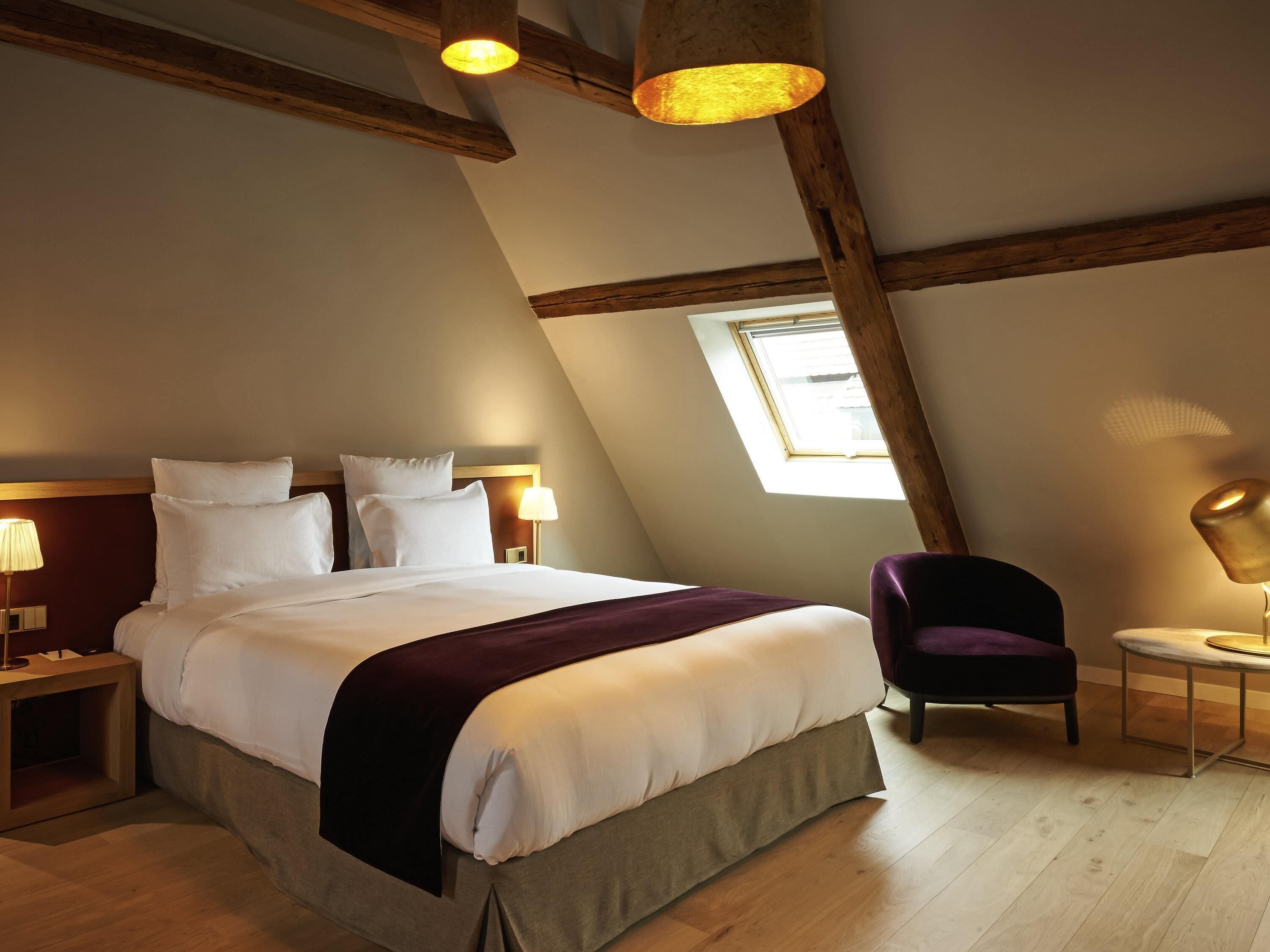 Ein Schlafzimmer mit einem großen Bett, Holzbalken, einem Oberlicht, einem Sessel und Nachttischlampen.