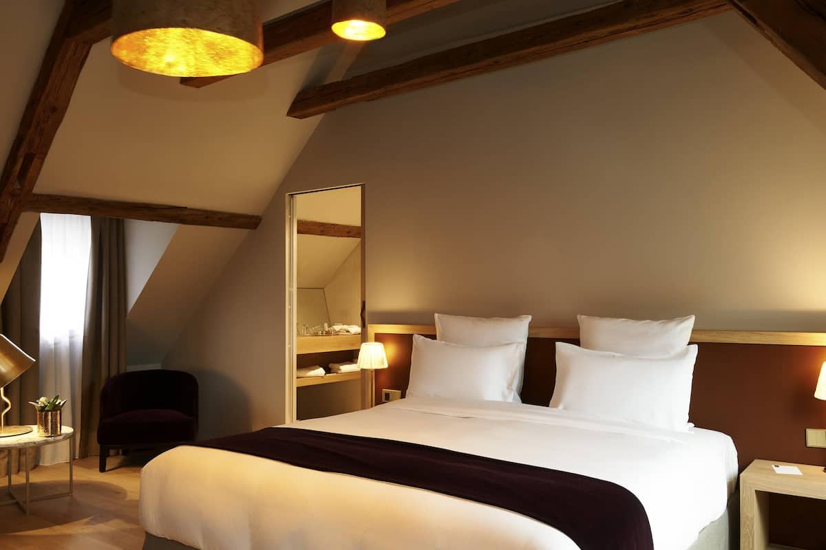 A hotel room with a large bed, a bedside table, a mirror, and a wooden ceiling.