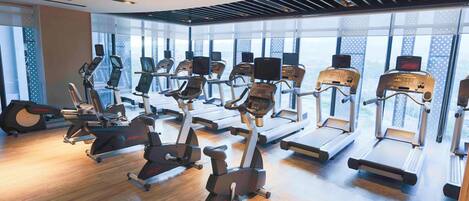 Un gimnasio con diversas máquinas de cardio, amplias ventanas y un diseño moderno.