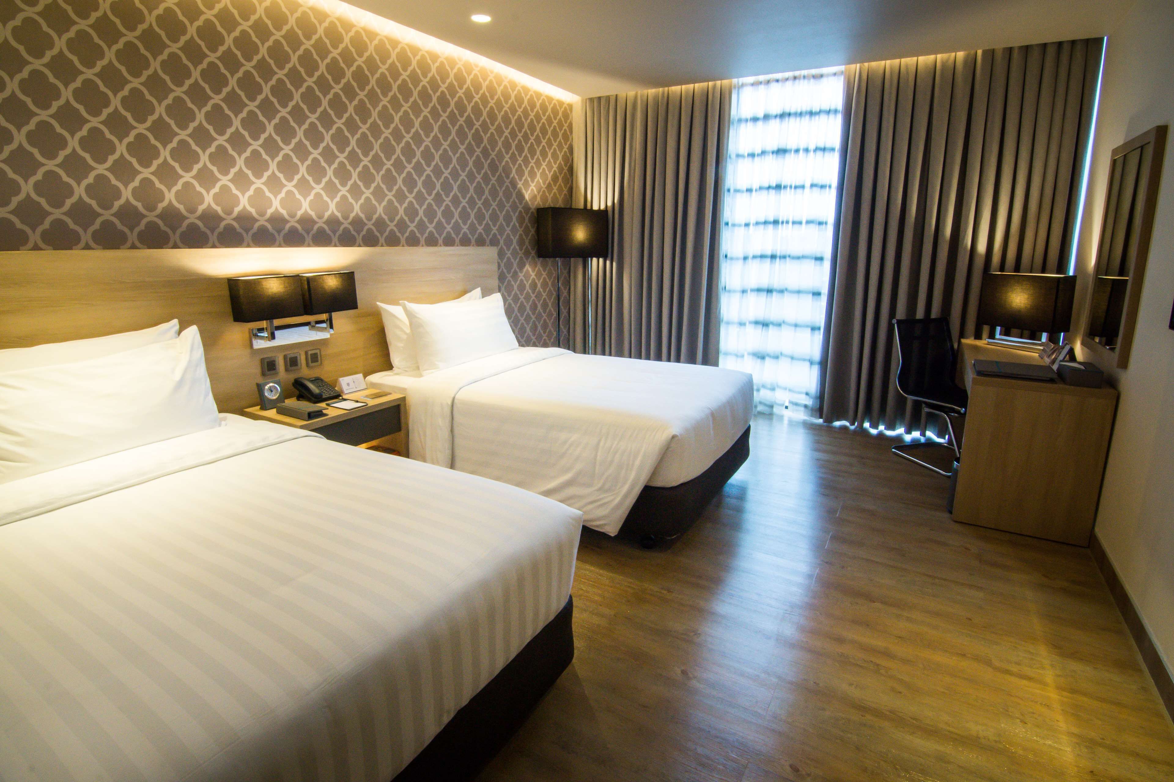 A hotel room with two beds, a TV, a desk with a lamp, and a large window with curtains.