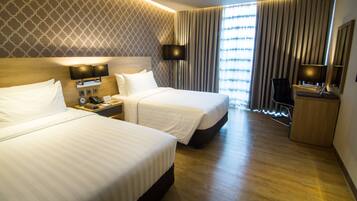 A hotel room with two beds, a TV, a desk with a lamp, and a large window with curtains.