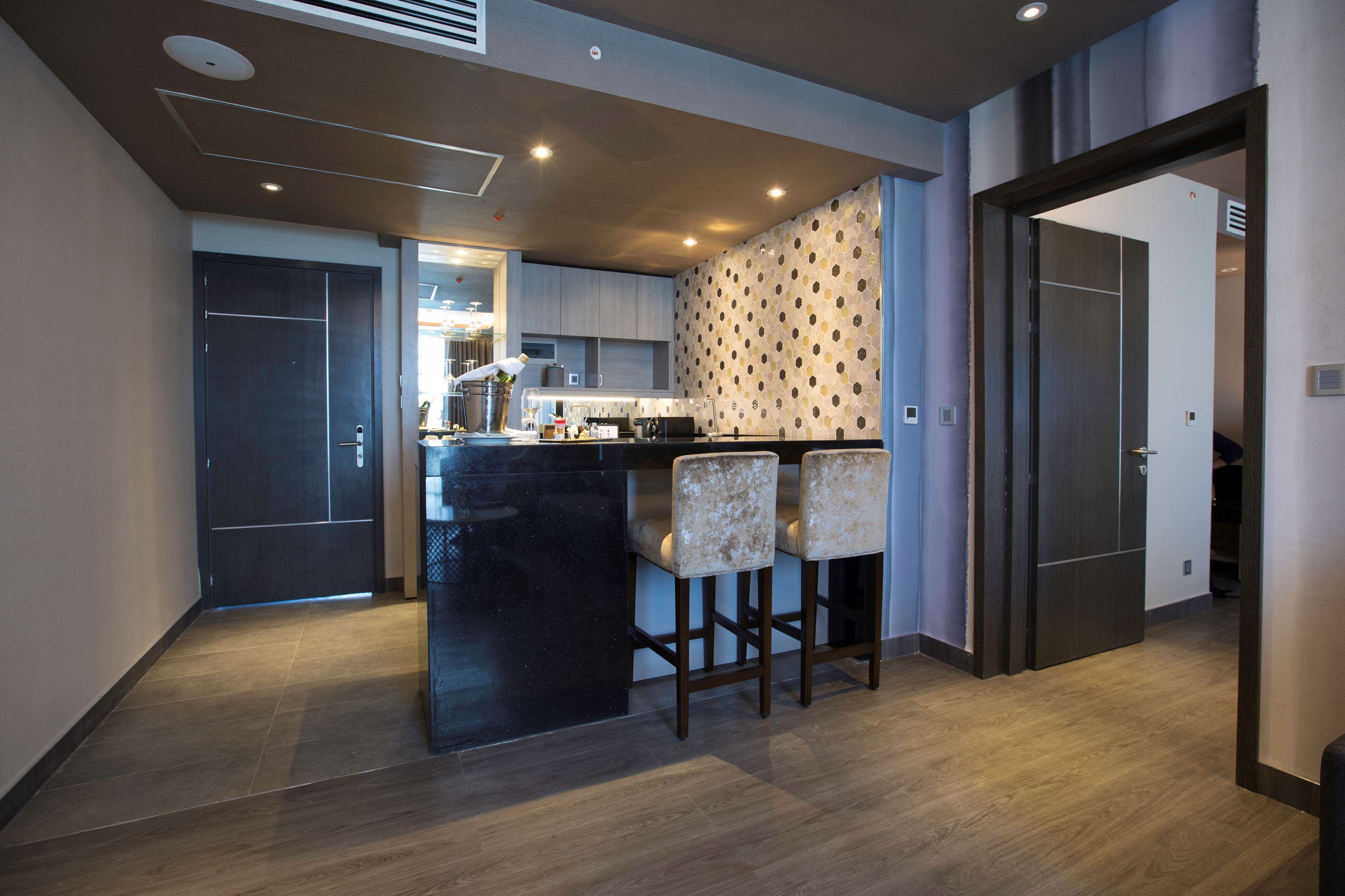 A modern kitchen with a central island, bar stools, and a patterned wall.